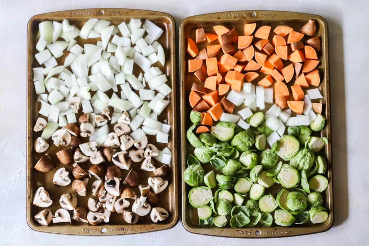 two baking sheets with mushrooms, onions, sweet potatoes, and brussels sprouts