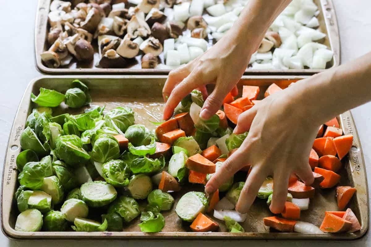 hands stirring together brussels sprouts, onions, and sweet potatoes on a baking sheet