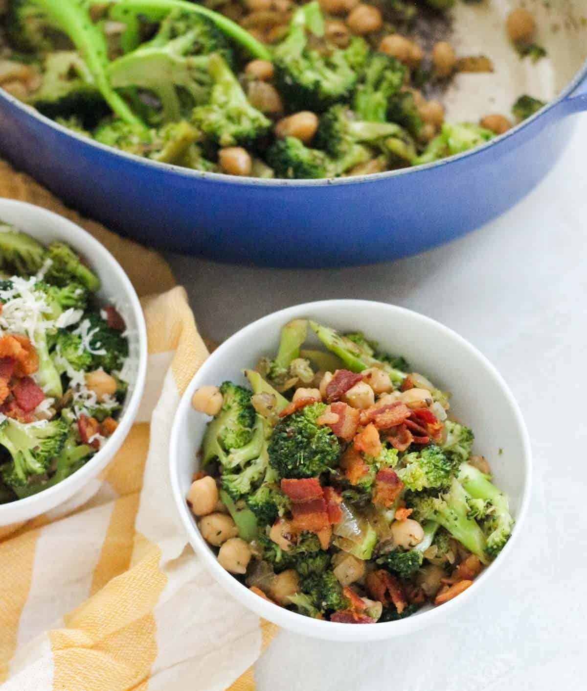 white bowls with bacon topped broccoli next to a blue pot and yellow and cream napkin