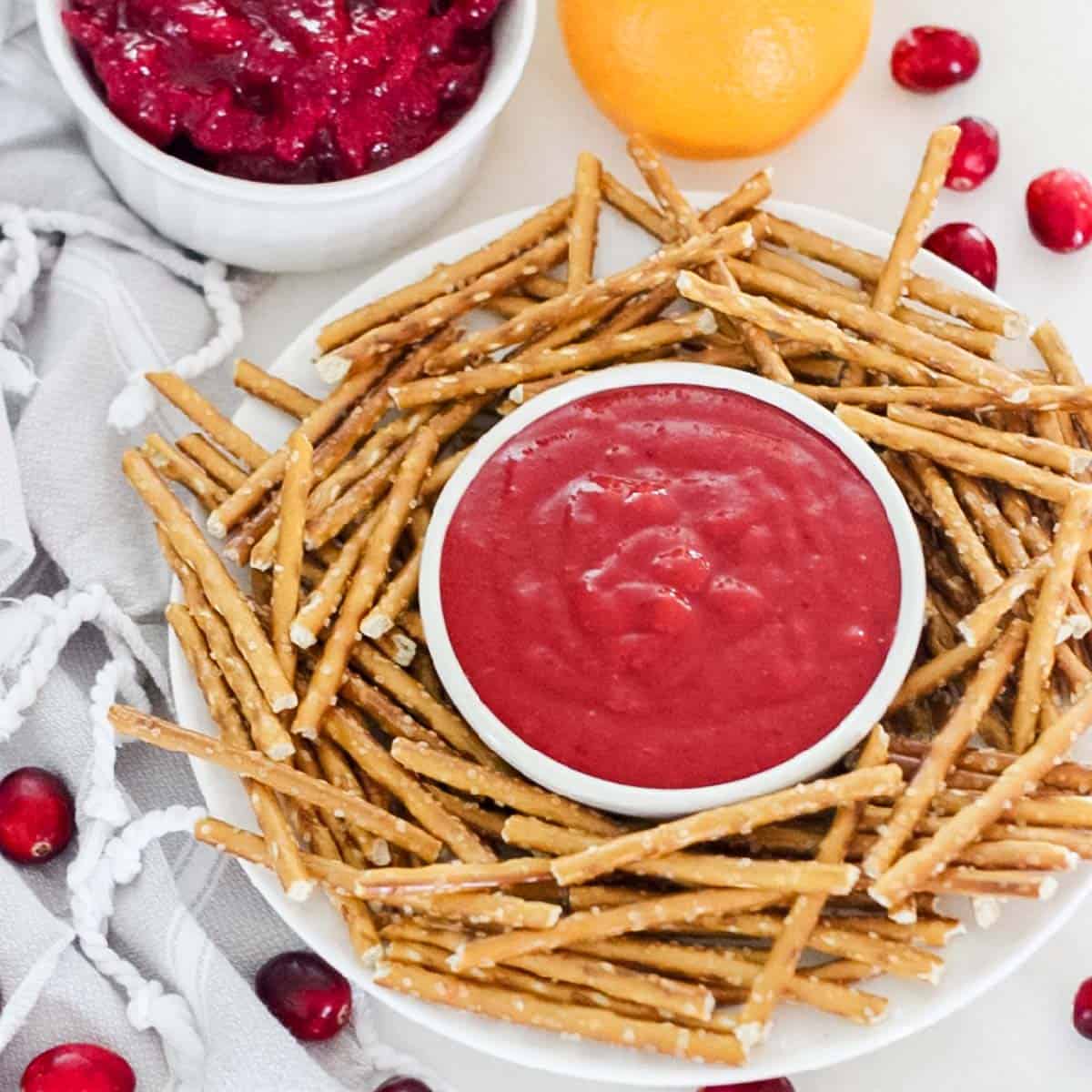 bowl of cranberry honey mustard sauce surrounded by pretzels and cranberries and cranberry sauce
