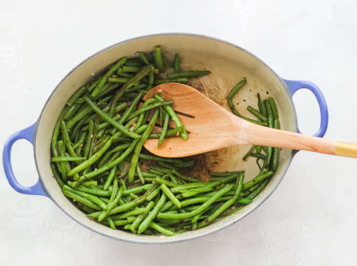 wooden slotted spoon stirring green beans in a blue pot