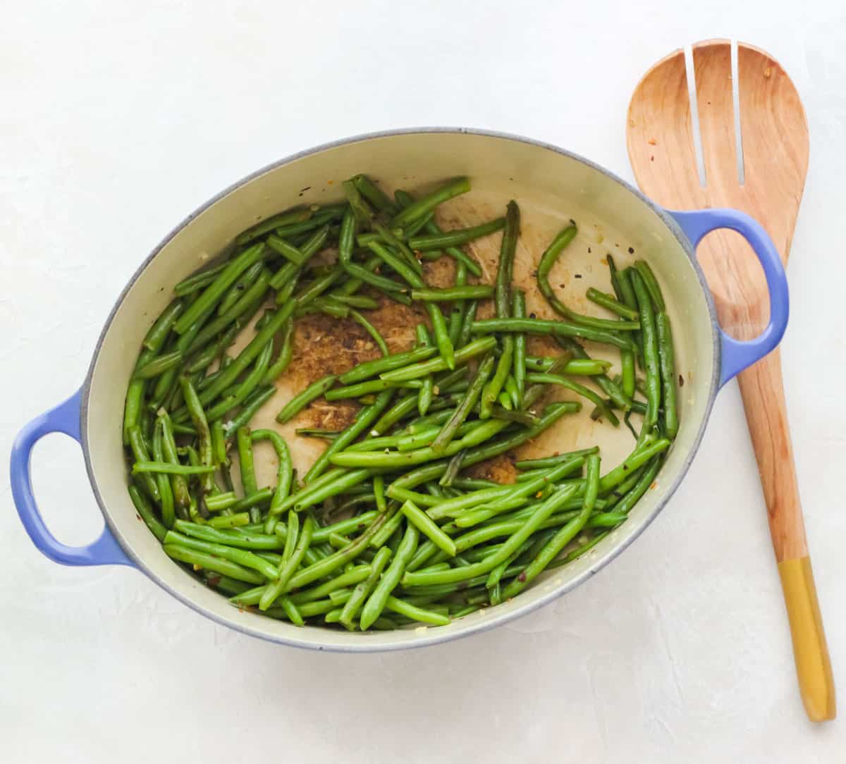blue pot with cooked green beans next to a wooden spatula on a white countertop