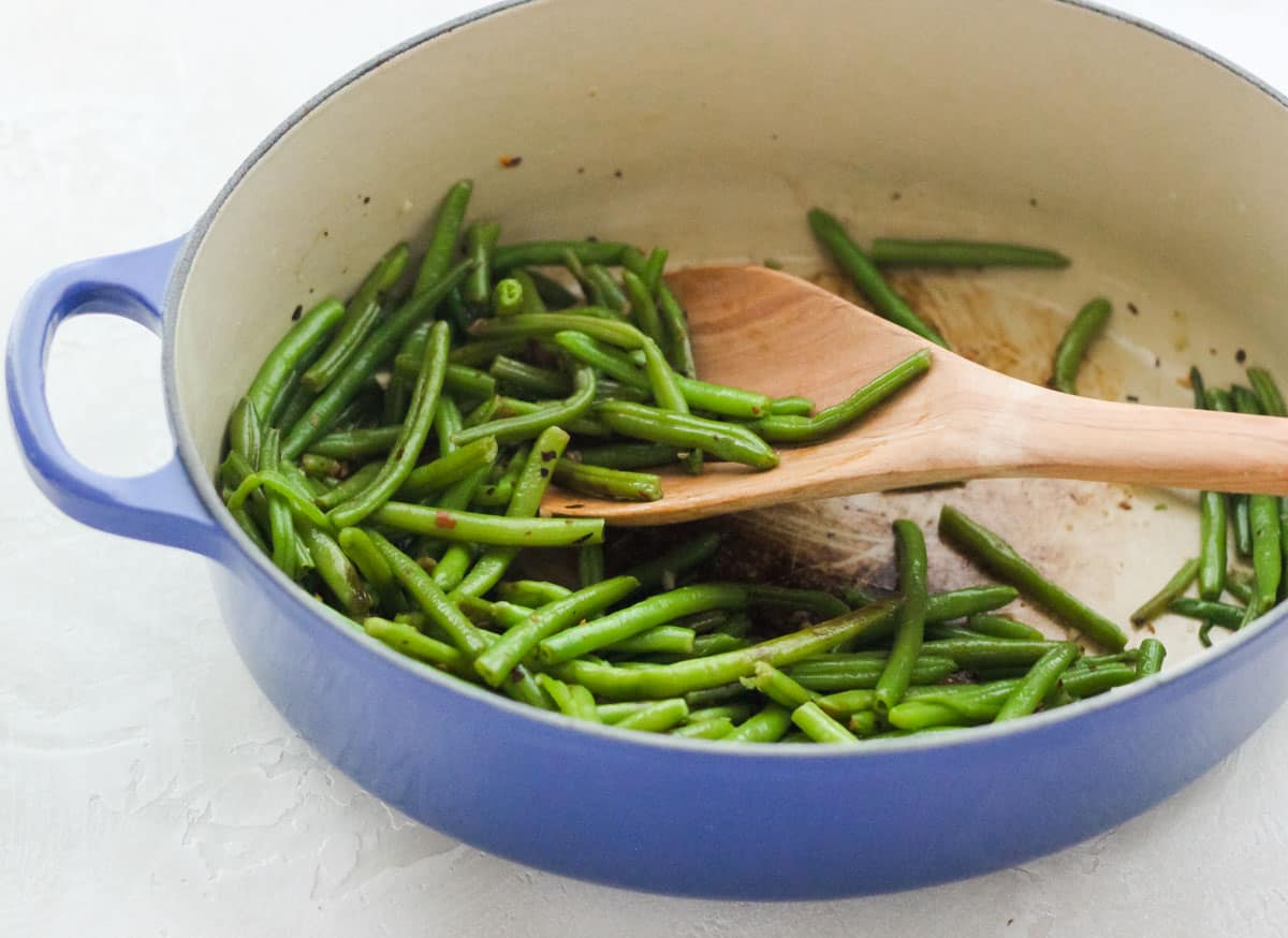 wooden spoon scooping up sauteed green beans out of a blue pot