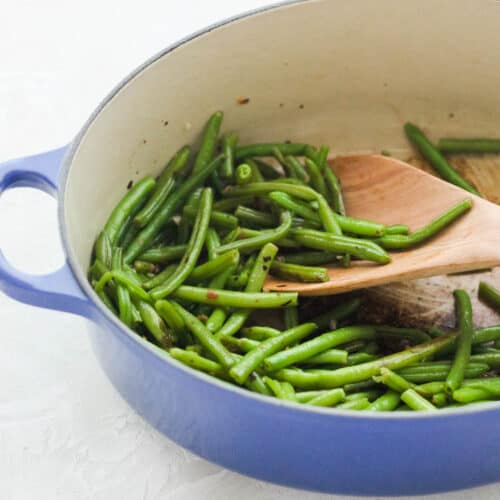 blue pot with sauteed green beans and a wooden spoon on a white countertop