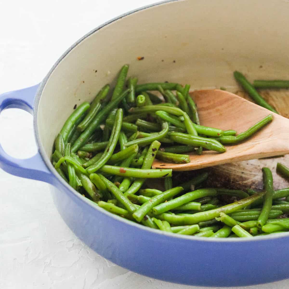 blue pot with sauteed green beans and a wooden spoon on a white countertop