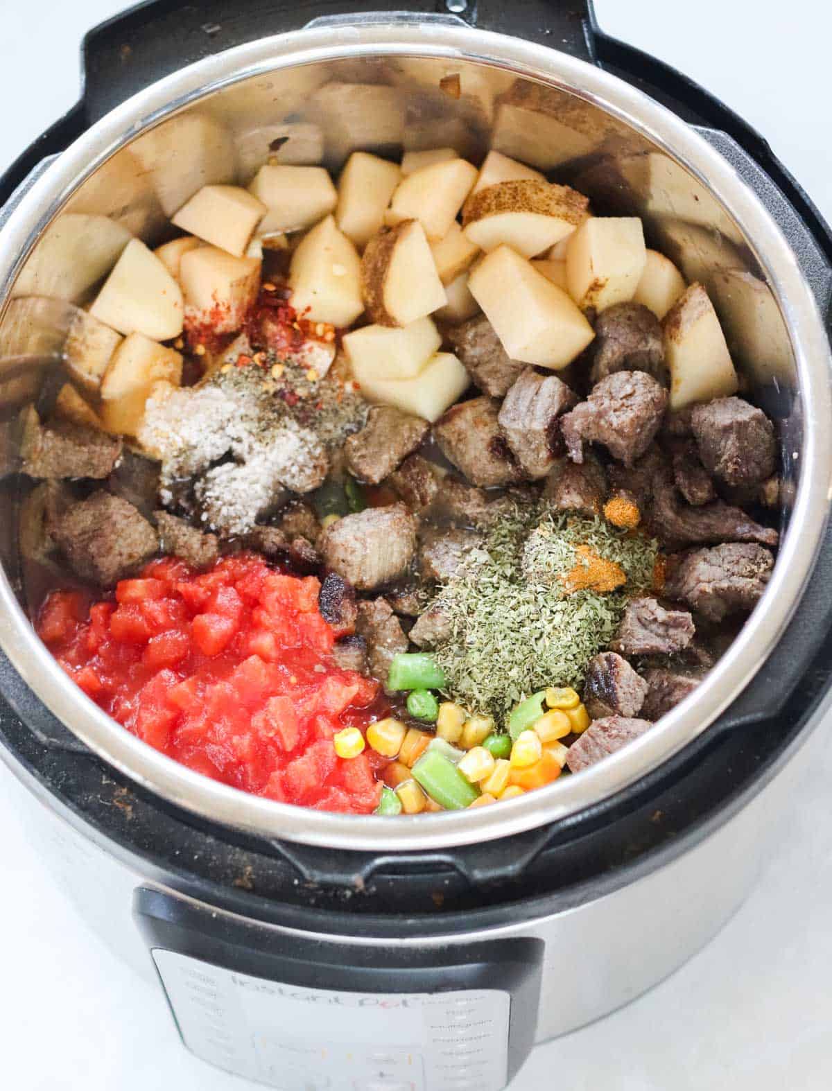 instant pot filled with potatoes, canned tomatoes, frozen mixed veggies, cooked beef, and spices before cooking