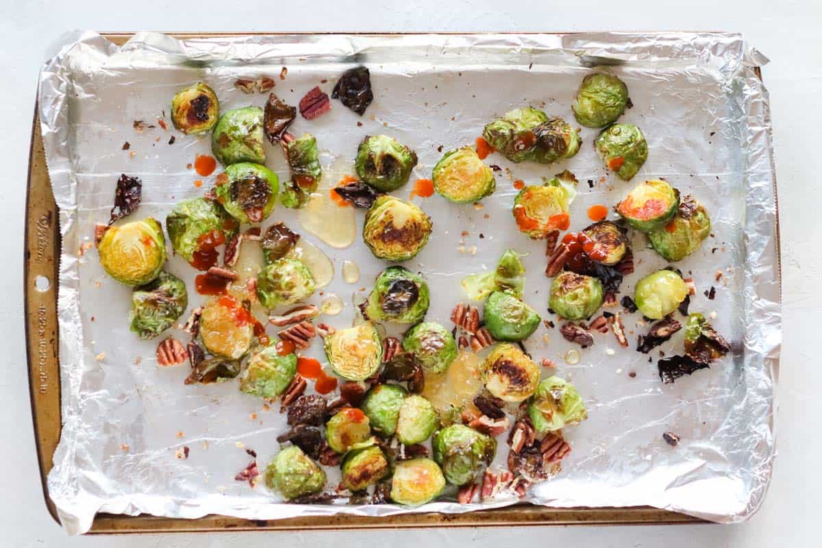 foil-lined baking sheet with roasted Brussels sprouts, pecans, covered in sriracha and honey
