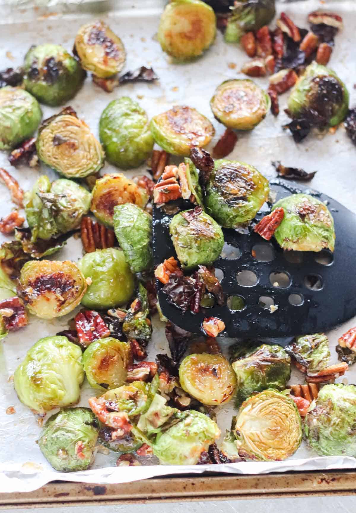 black spatula stirring roasted Brussels sprouts, pecans, honey, and sriracha sauce