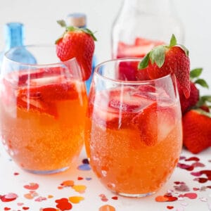 two glasses of strawberry gin fizz surrounded by valentines day confetti and strawberries