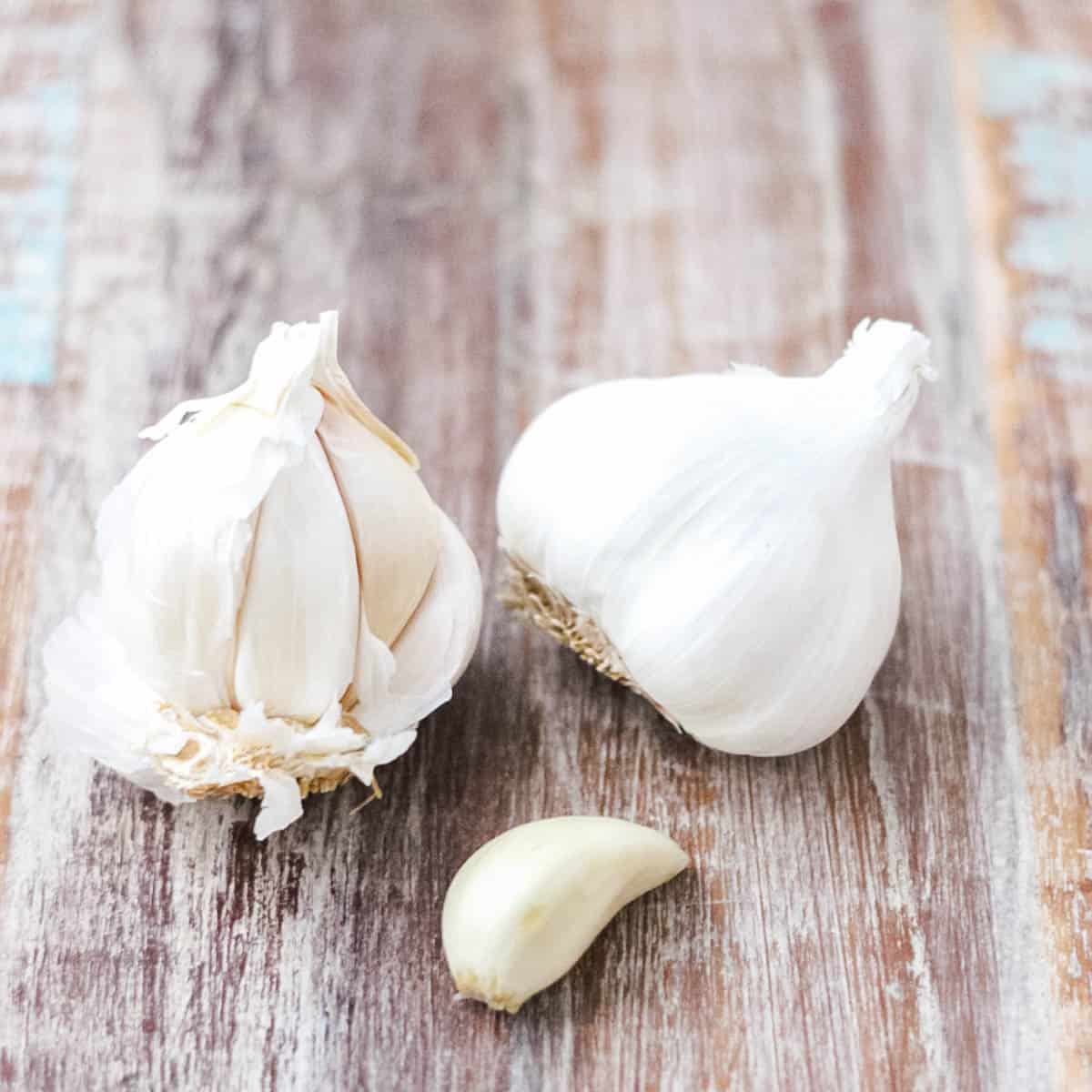 garlic clove next to two heads of garlic on a wooden table