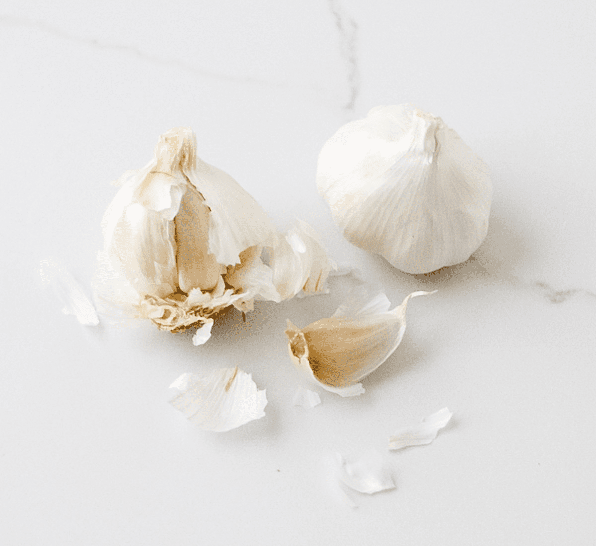 garlic cloves and garlic skin on white marble counter