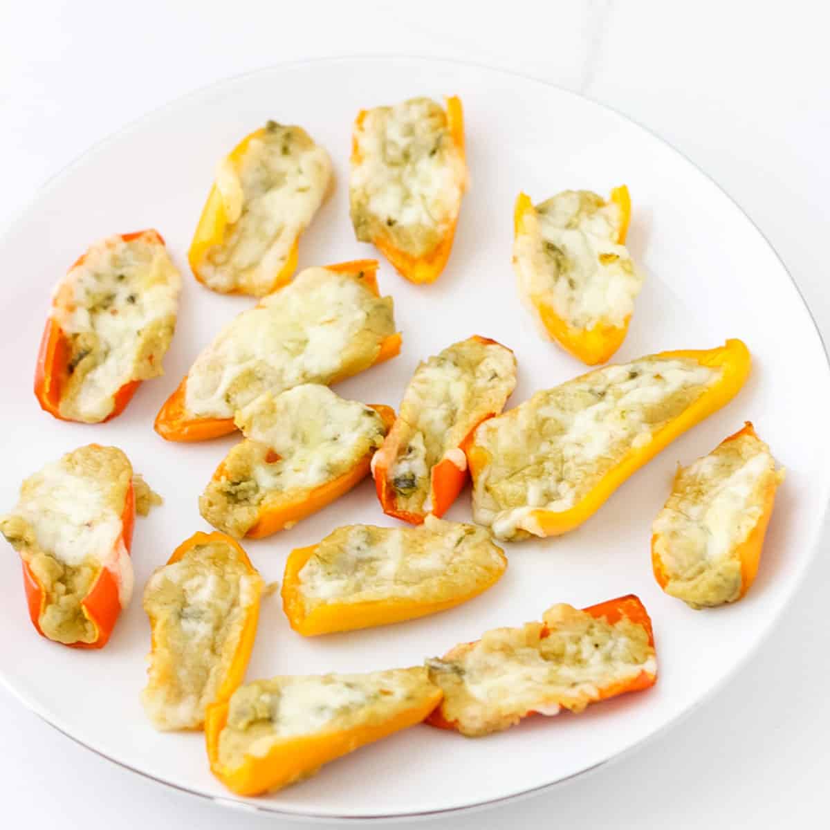 white plate with red, yellow, and orange mini peppers stuffed with hummus and topped with cheese then baked