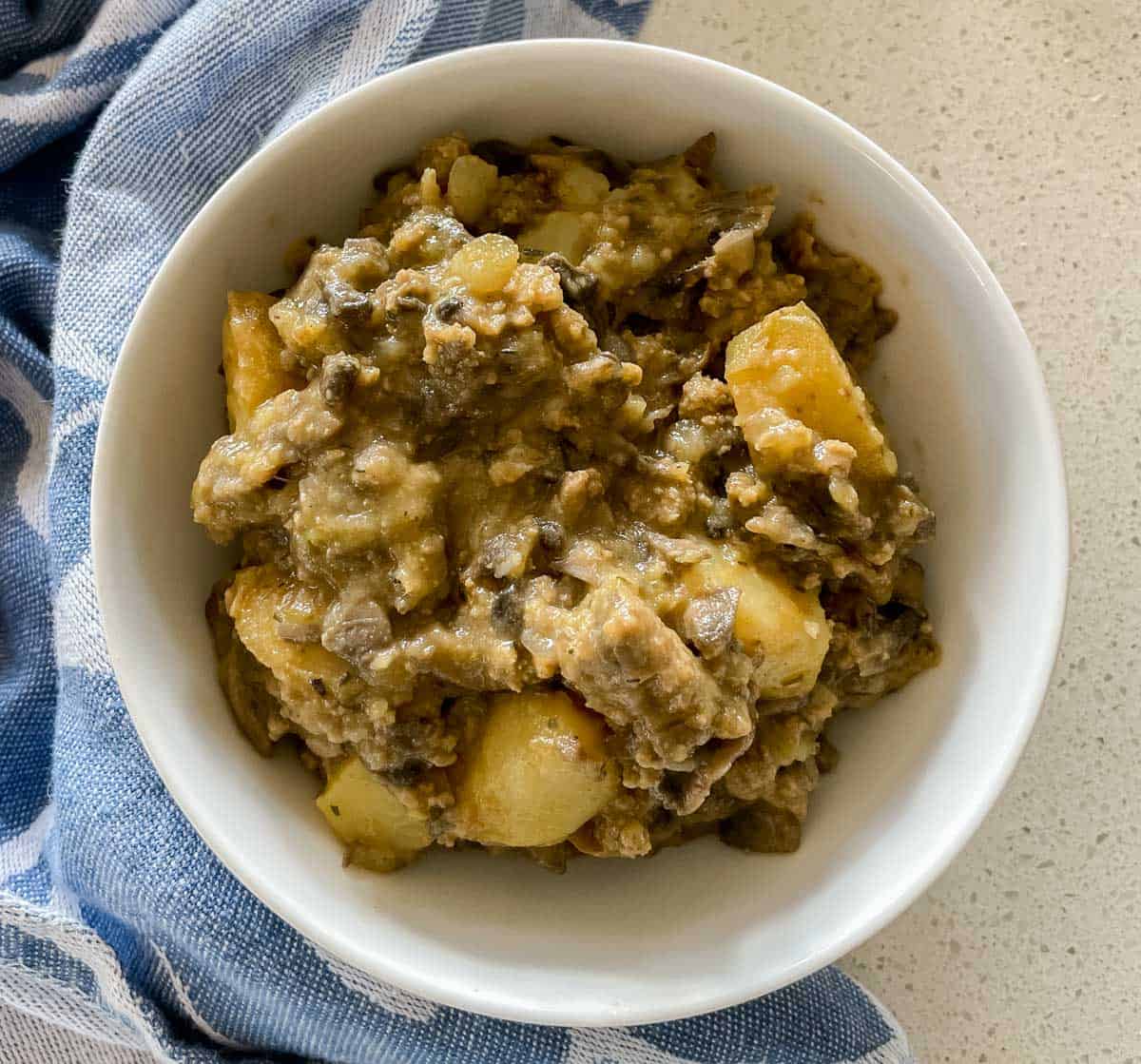 bowl of sausage mushroom hash in a white bowl on a white countertop with a blue dish towel