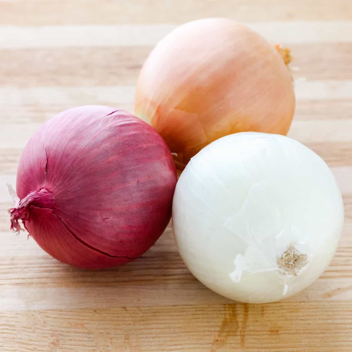 wooden cutting board with one each of red, white, and yellow onions