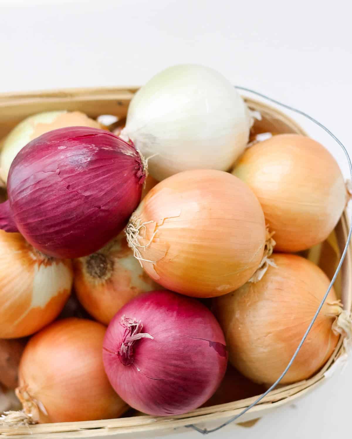 yellow, red, and white onions in a wooden basket