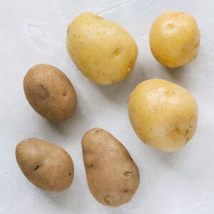 three golden potatoes and three russet potatoes on a white countertop