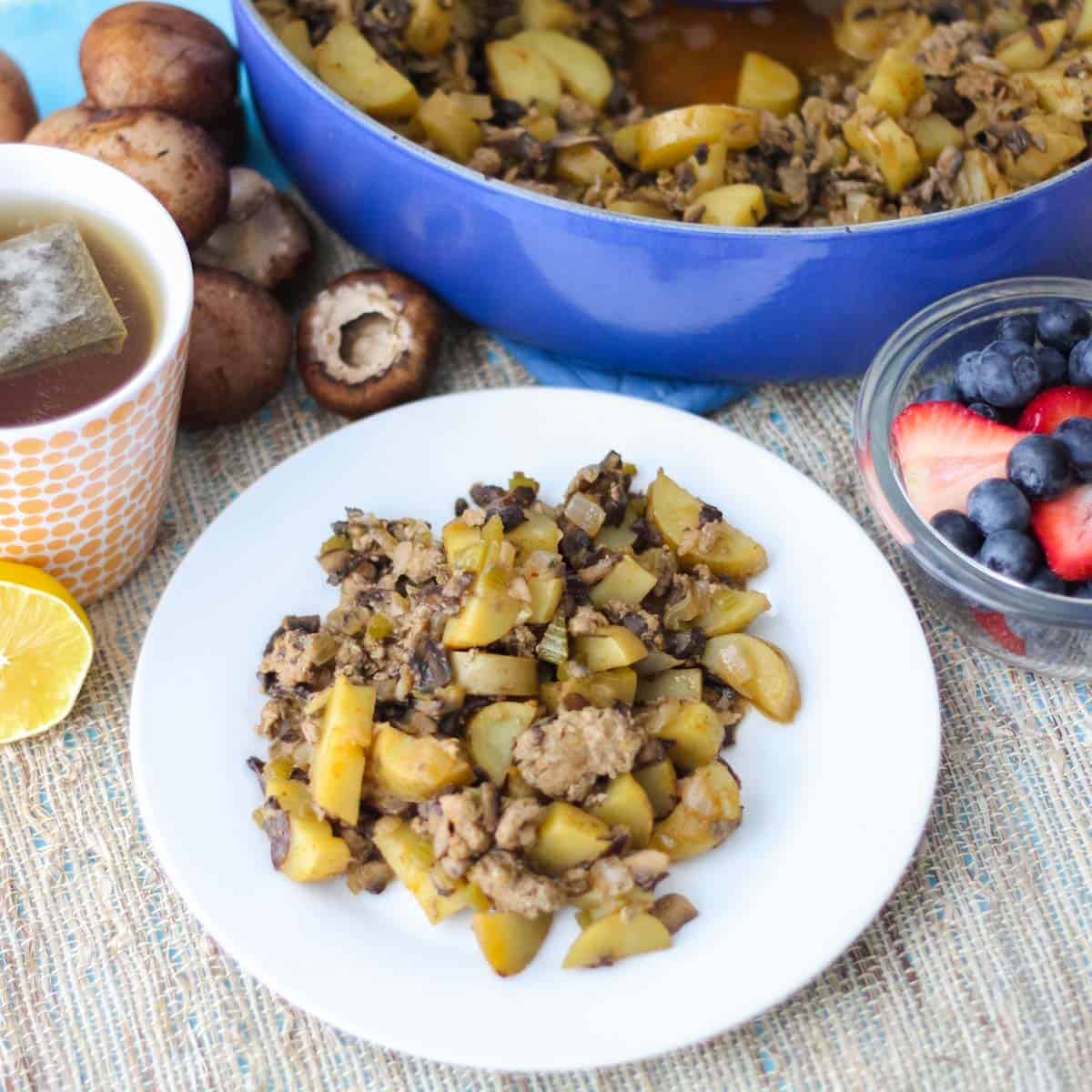 blue pot with sausage hash, cup of tea, bowl of berries, white plate with hash