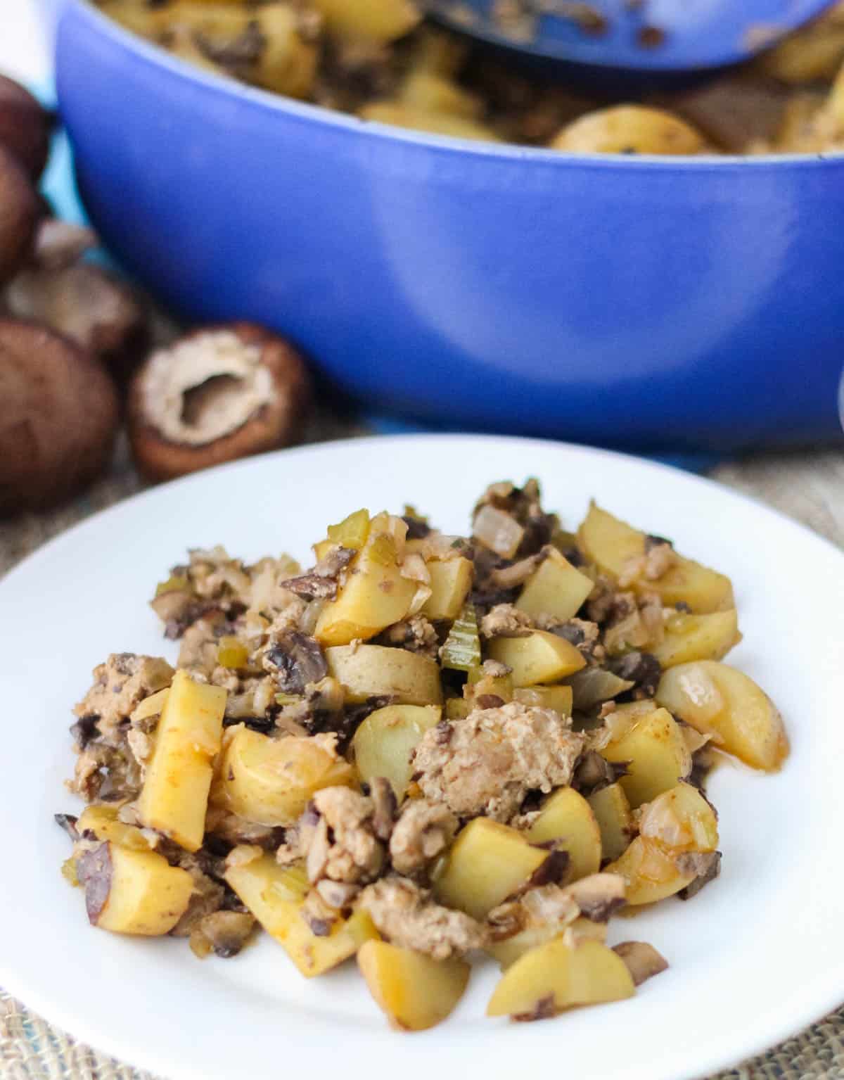 white plate with ground turkey, mushrooms, and potatoes with a blue pot and mushrooms in background