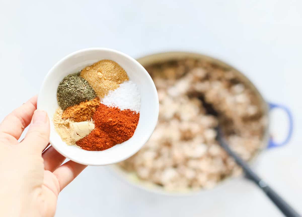 hand holding a small bowl of spices over a pot