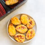 basket of an air fryer with a potato inside next to a plate of twice baked potatoes