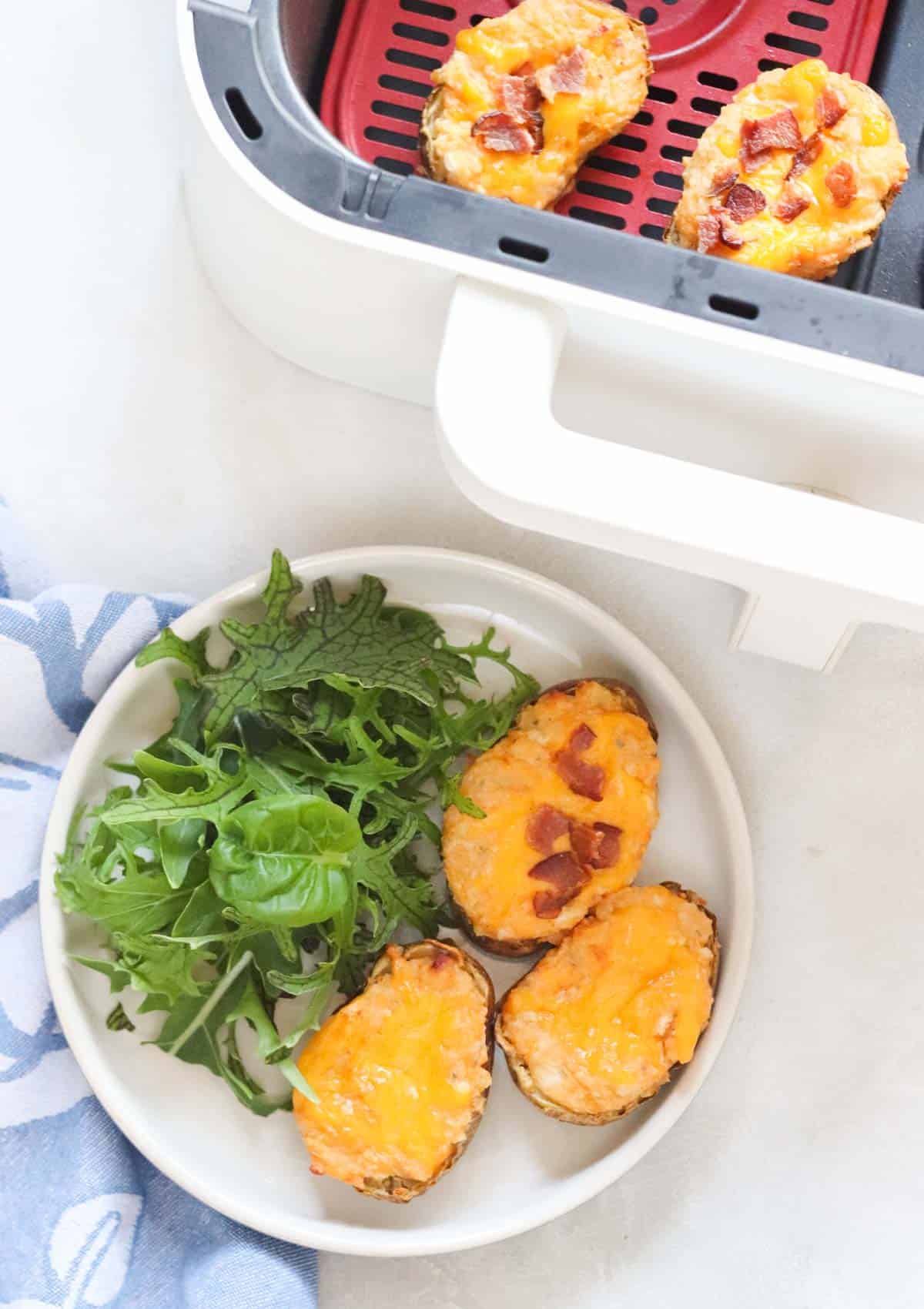 twice baked potatoes and a salad on a plate next to an air fryer basket with more twice baked potatoes