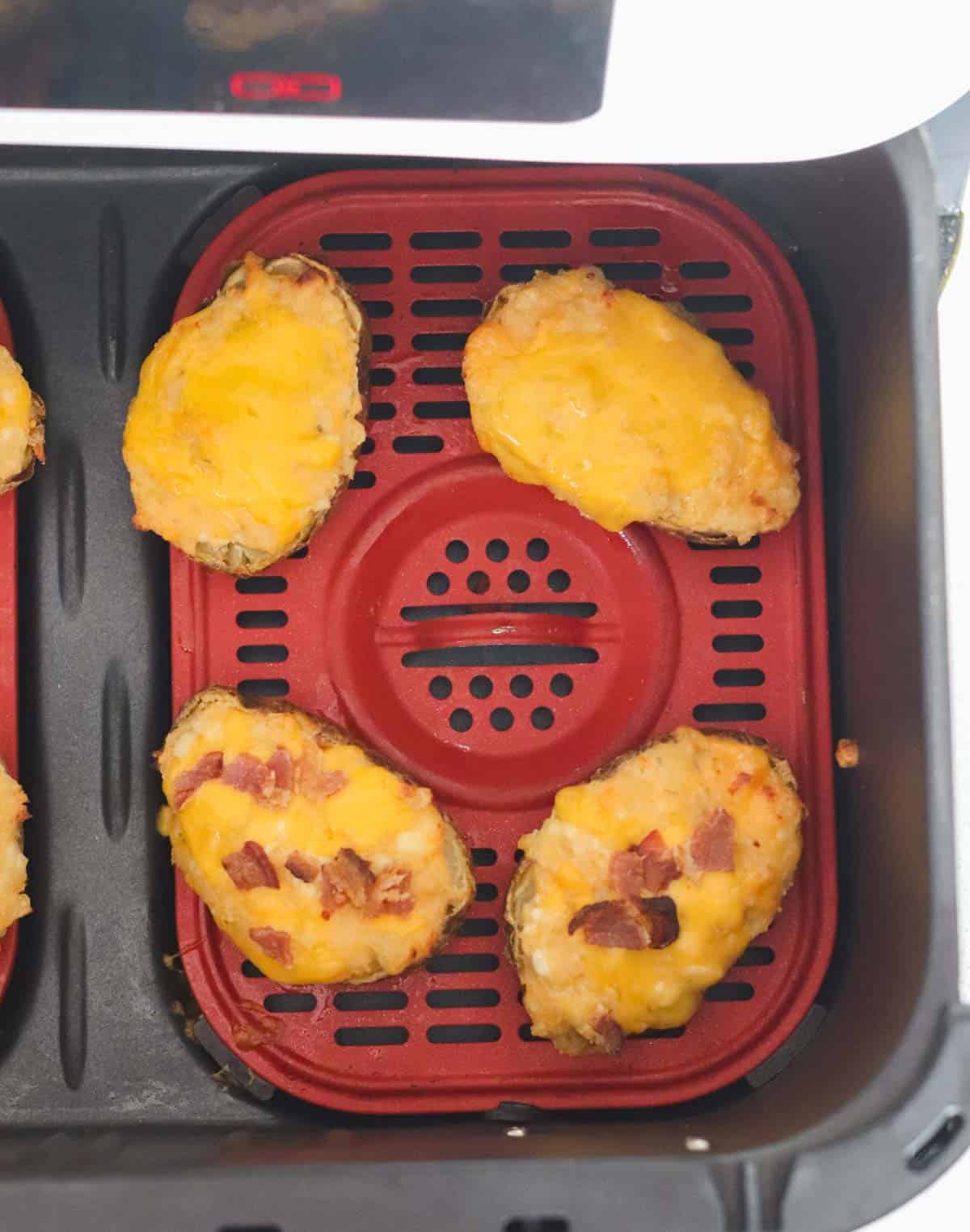 four twice baked potatoes, two topped with bacon, sitting in the basket of an air fryer after being cooked