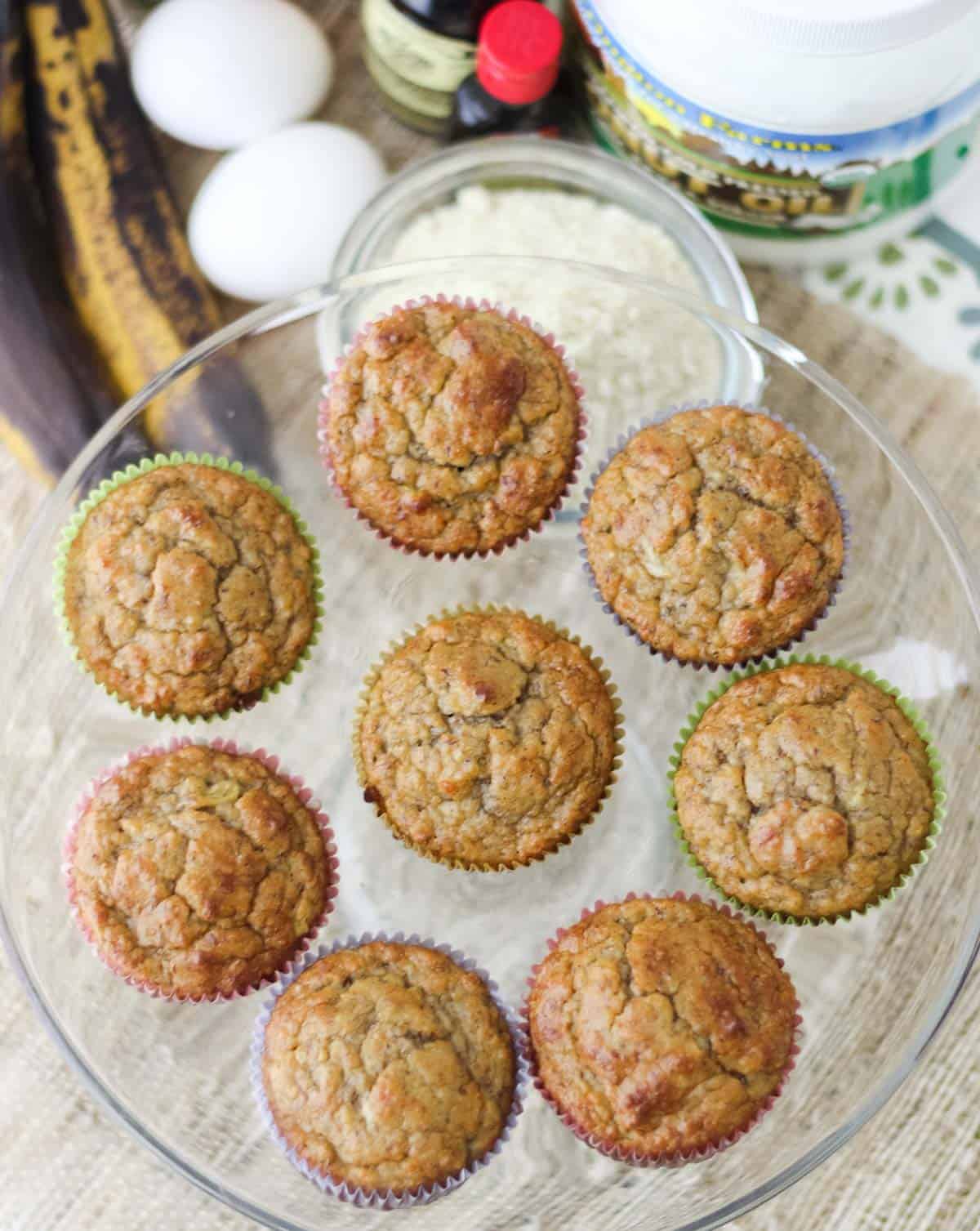 overhead photo of muffins on a glass plate with almond flour, bananas, eggs, and coconut oil
