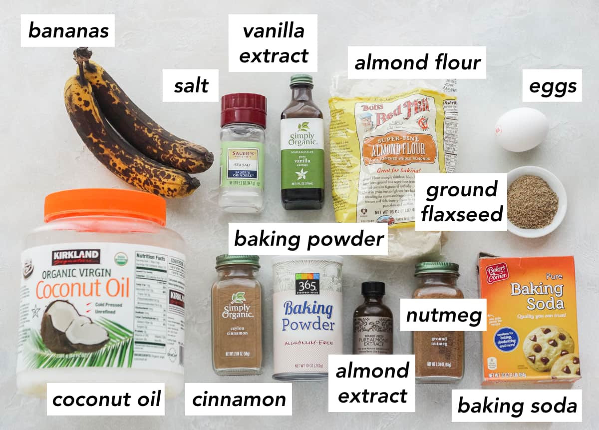 two ripe bananas, tub of coconut oil, ground cinnamon, container of baking powder, bottle of almond extract, ground nutmeg, box of baking soda, bowl of flaxseed, one egg, bag of almond flour, bottle of vanilla extract, salt