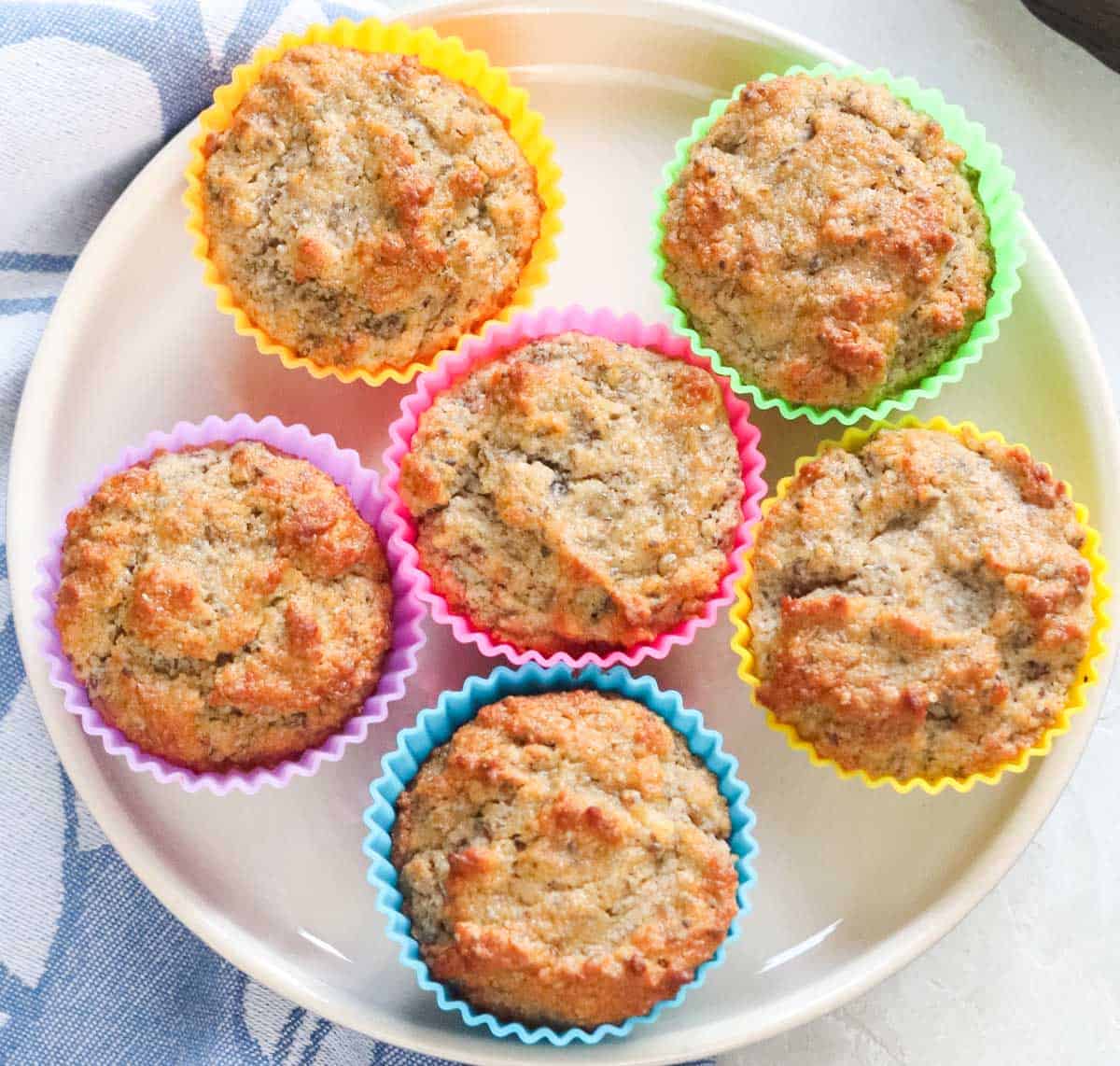 overhead view of six muffins with colorful silicone liners next to a blue napkin