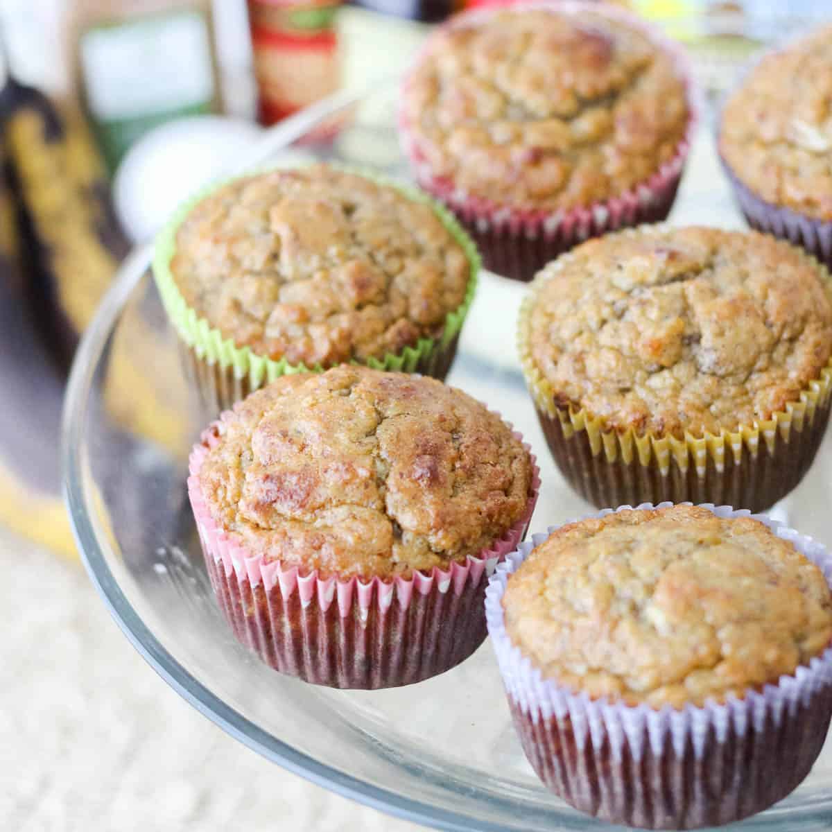 clear plate of almond banana muffins in colorful paper cupcake liners with ingredients blurry in the background