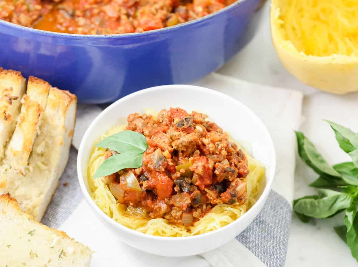 bowl of Turkey Meat Sauce with spaghetti squash, basil, and garlic bread next to a pot of sauce
