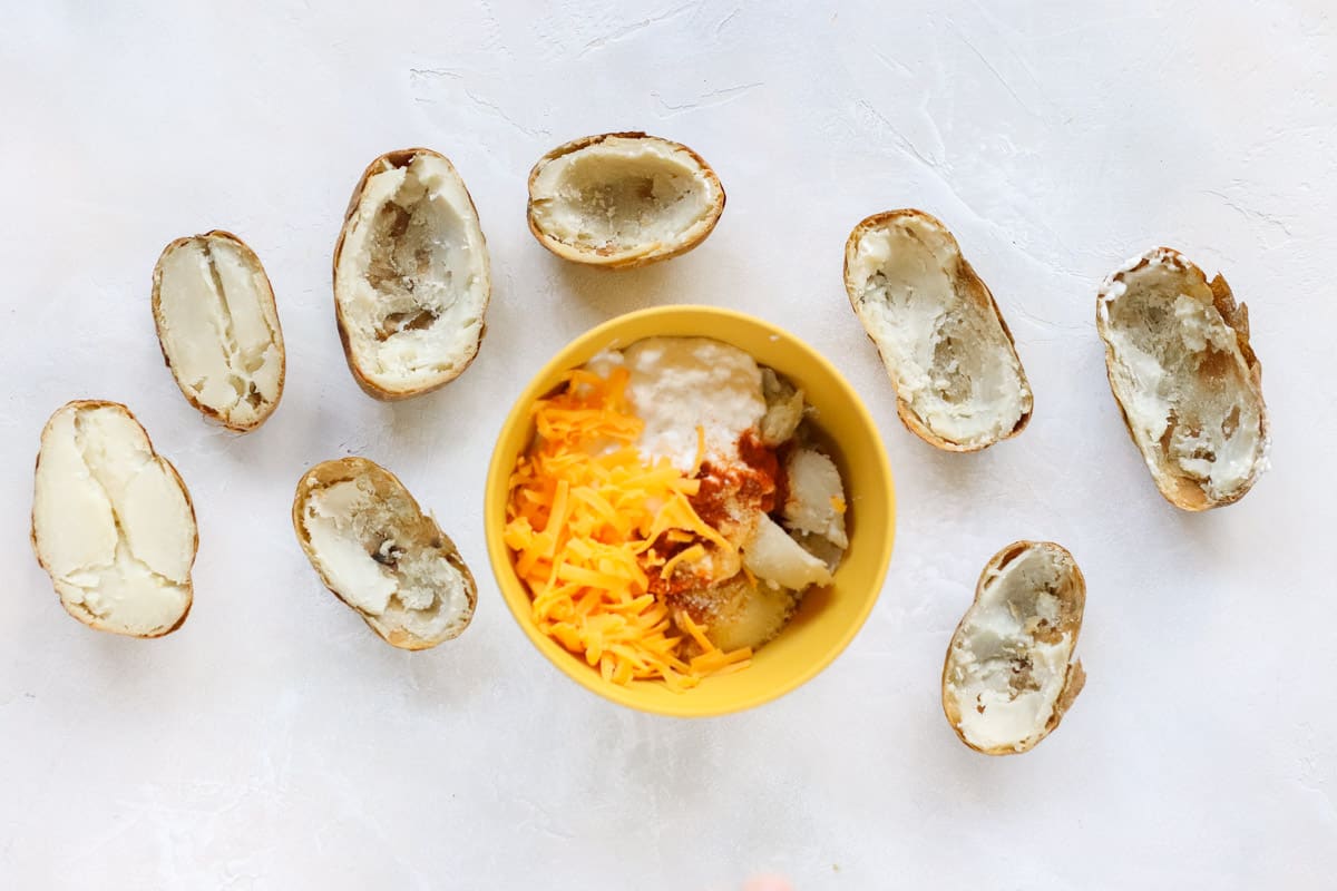 baked potato halves surrounding a bowl with cottage cheese, cheddar cheese, spices, and potato flesh