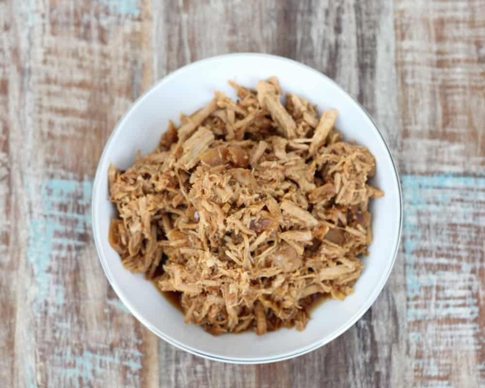 bowl of shredded pork loin on a wooden table.