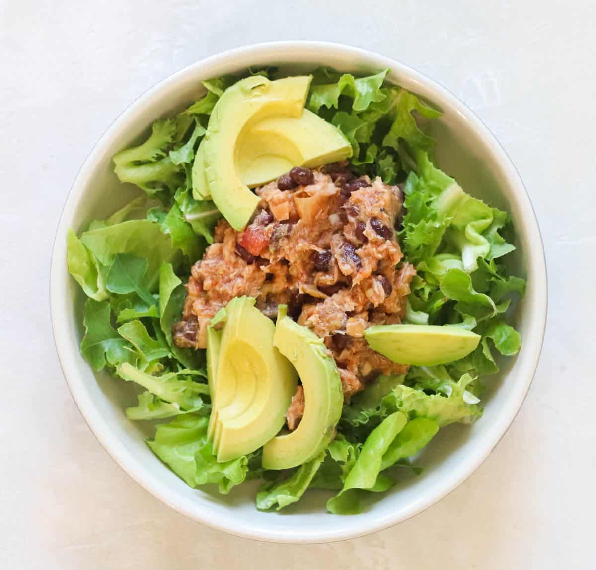 bowl of lettuce topped with salsa tuna salad black beans and avocados.