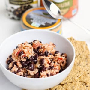 white bowl with black bean salsa tuna salad surrounded by crackers and a can of tuna, black beans, and jar of salsa in background.