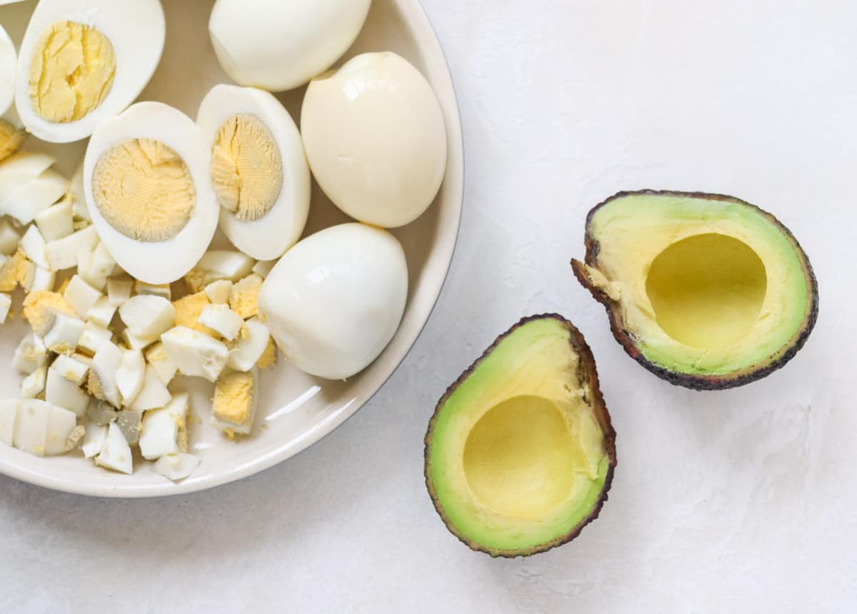 plate of hardboiled eggs halved and chopped next to a cut avocado.