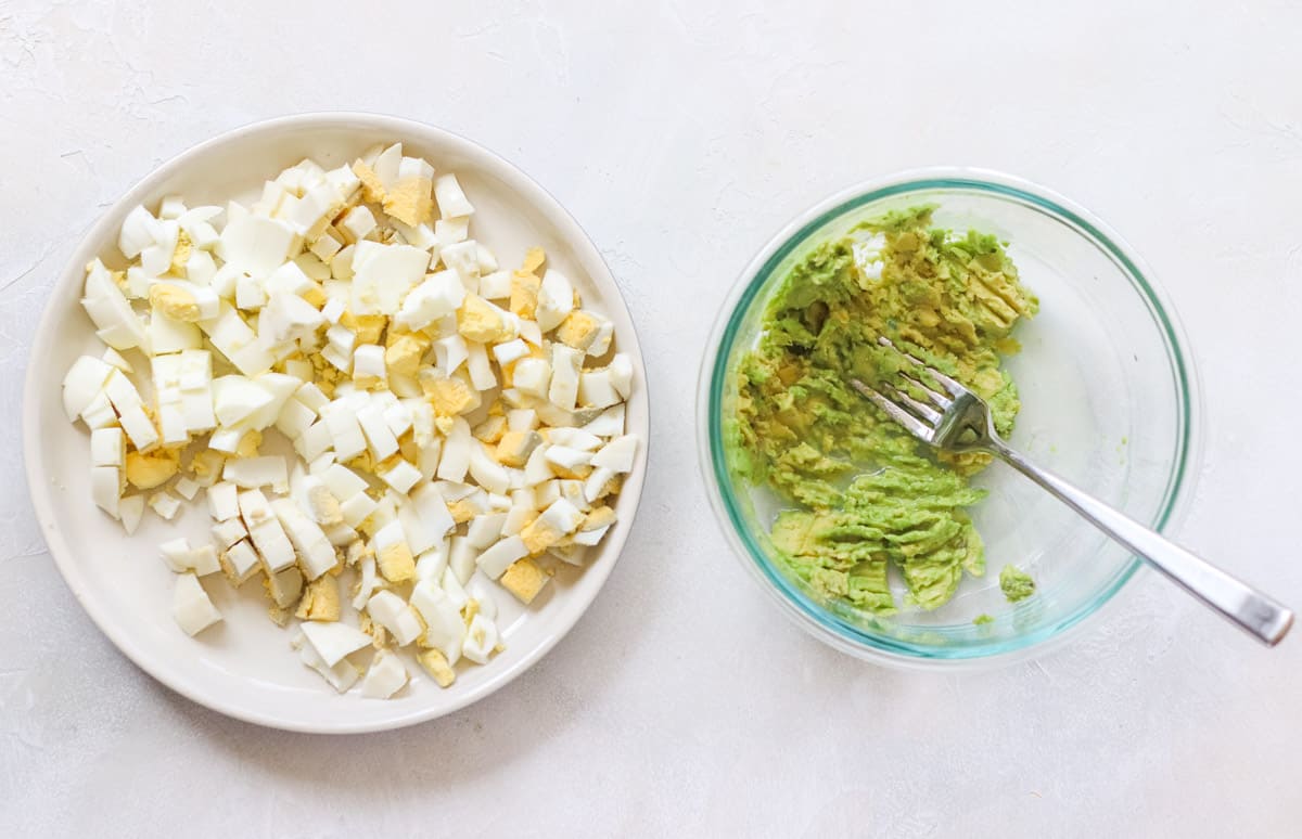 plate of chopped hardboiled eggs next to a bowl with mashed avocado and silver fork.