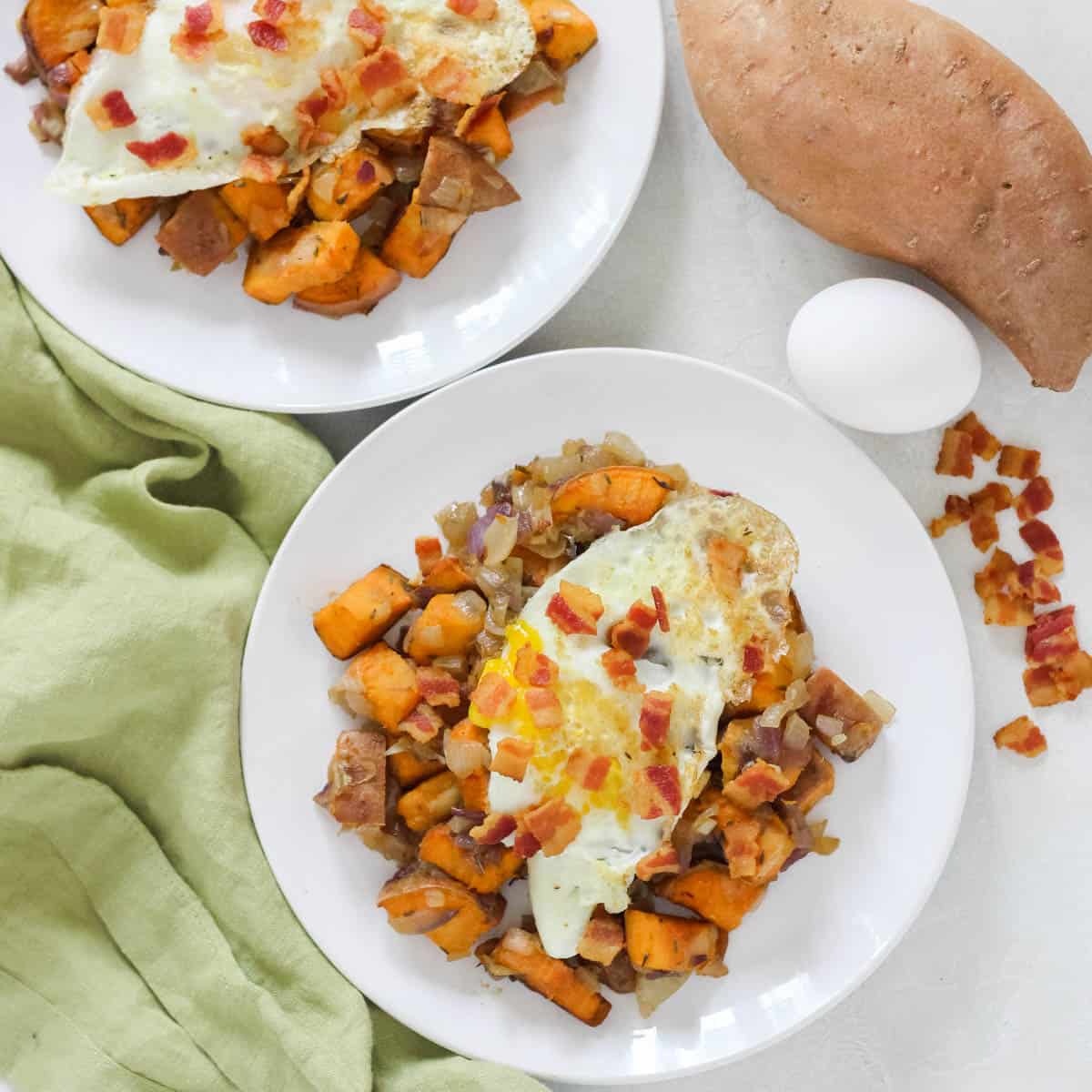 green napkin, sweet potato, bacon crumbles, egg, two plates with sweet potato bacon hash topped with fried eggs.
