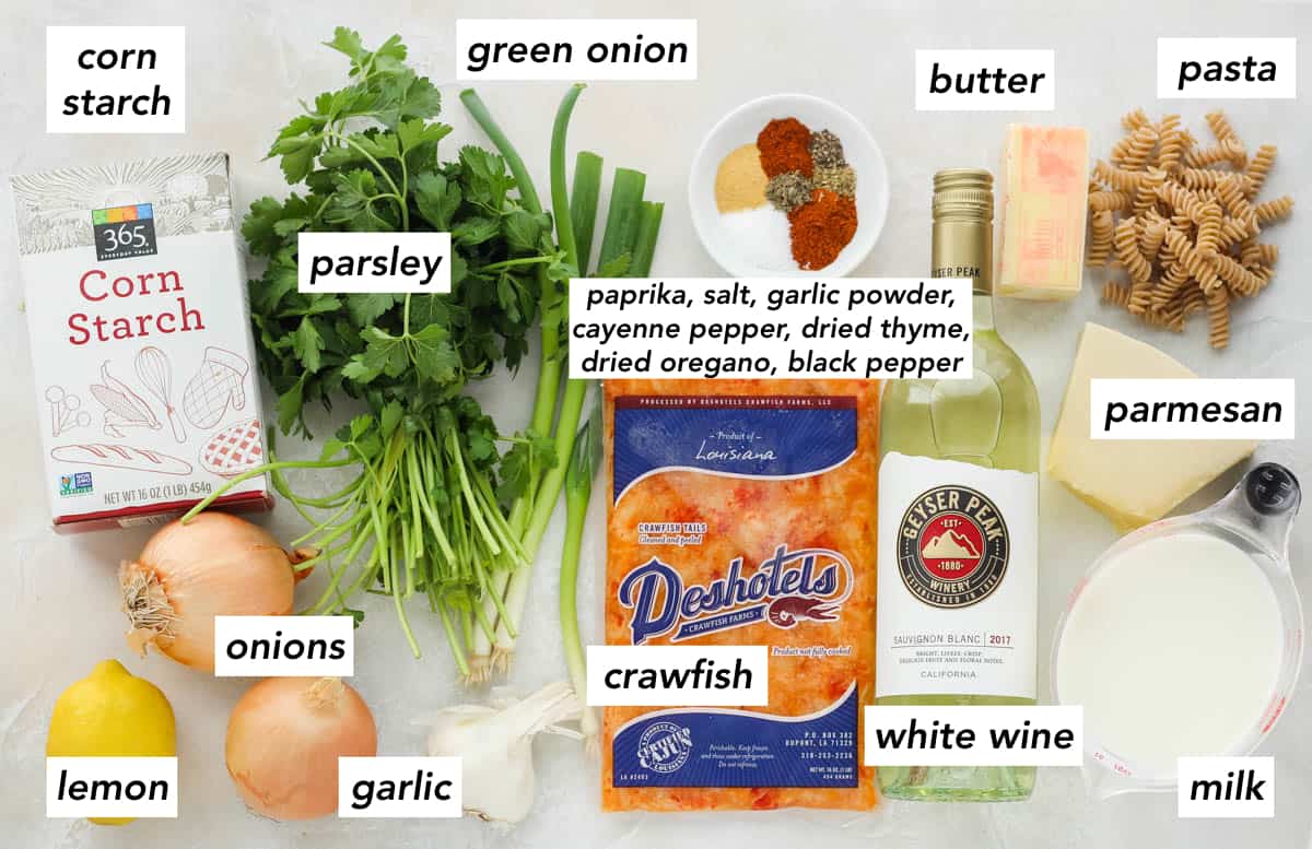 lemon, two onions, box of cornstarch, parsley, green onions, garlic, crawfish, bowl of spices, wine, butter, pasta, parmesan, milk.