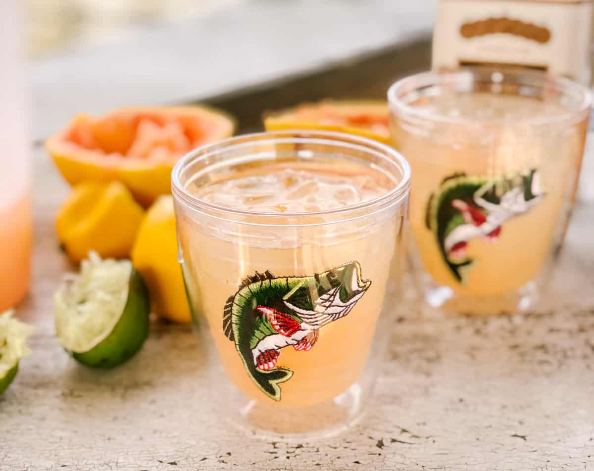 distressed wooden table with lemon, limes, and grapefruits with two glasses of grapefruit margaritas.