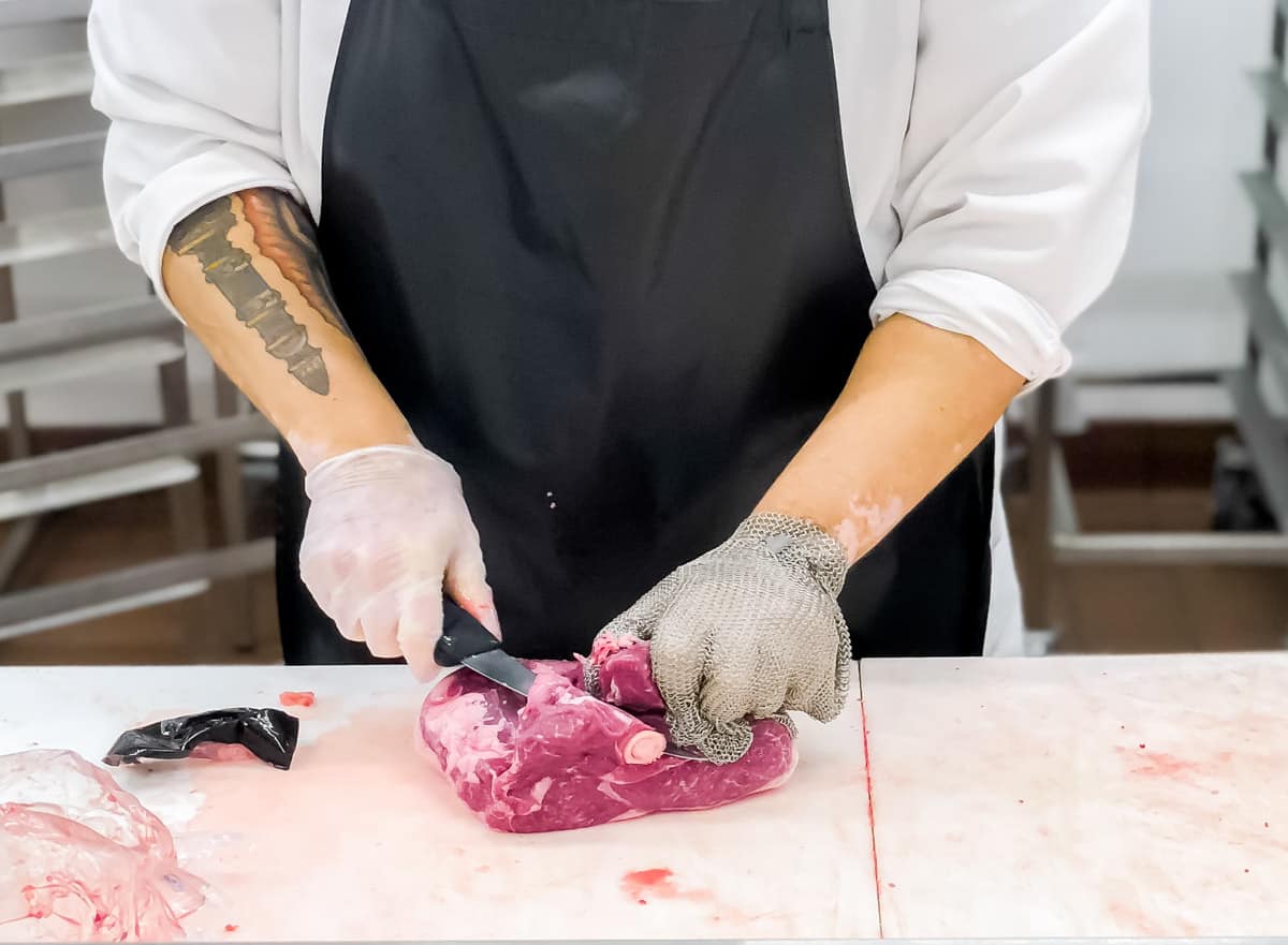 butcher cutting a bone-in lamb shoulder at the grocery store.