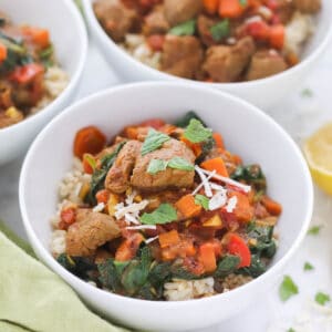 close up of a bowl of lamb curry over rice sprinkled with mint and coconut flakes.