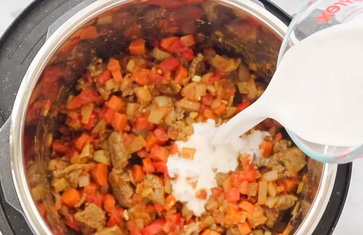 coconut milk being poured over sauteed veggies in an instant pot.