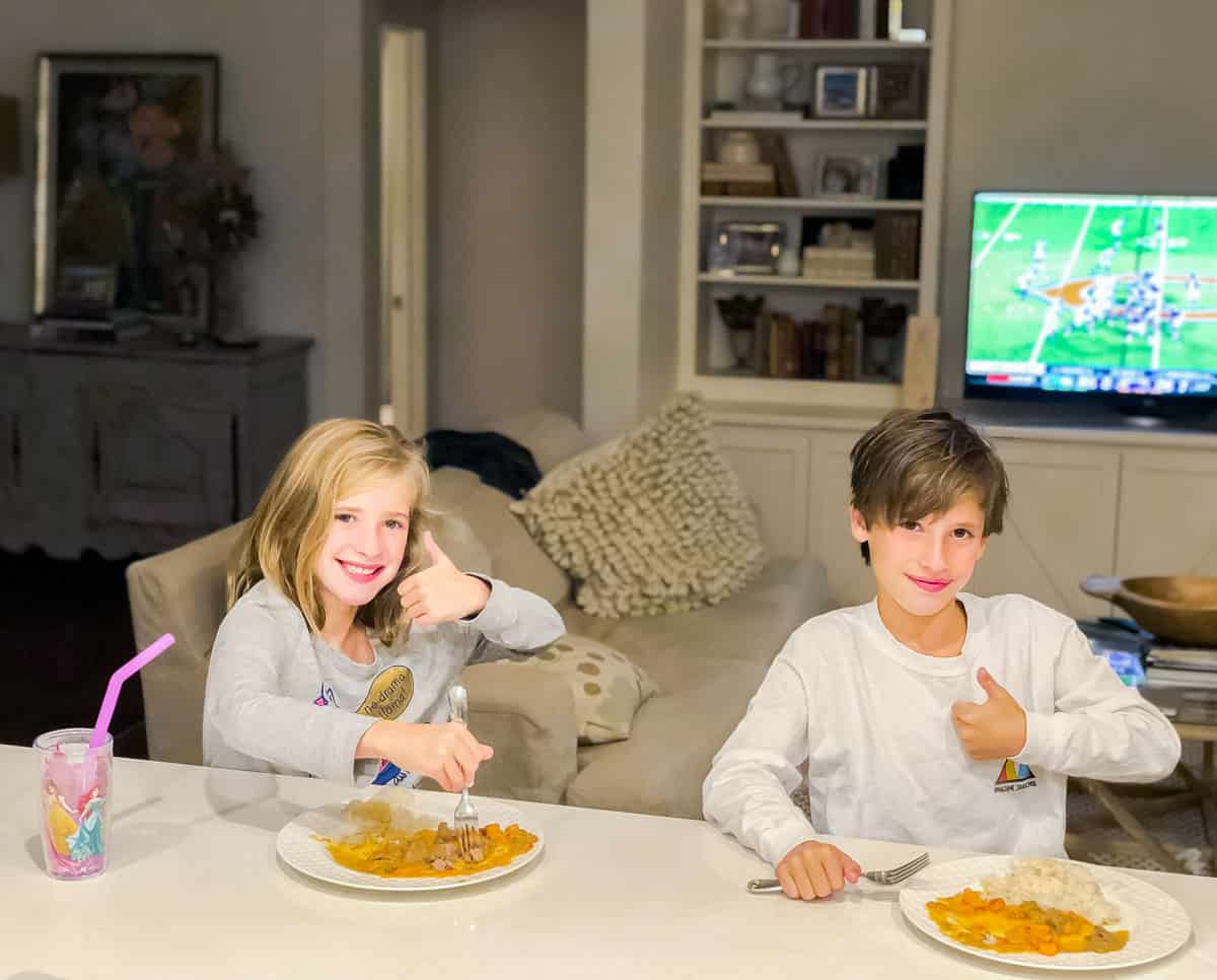 two kids giving the camera a thumbs up while eating rice and curry.