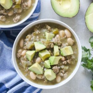 bowl of turkey white bean chili topped with fresh avocado next fresh avocado and cilantro.