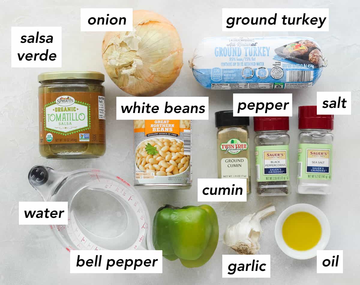 tomatillo salsa jar, cup of water, green bell pepper, garlic, small bowl of oil, salt, black pepper, cumin, can of white beans, package of ground turkey, yellow onion.