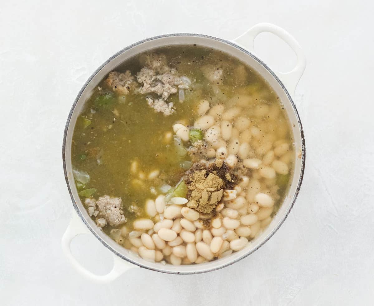 tan pot with ground turkey, cumin, white beans, and green salsa being cooked.