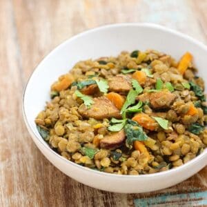 wooden table with white bowl of sausage lentil casserole with kale.