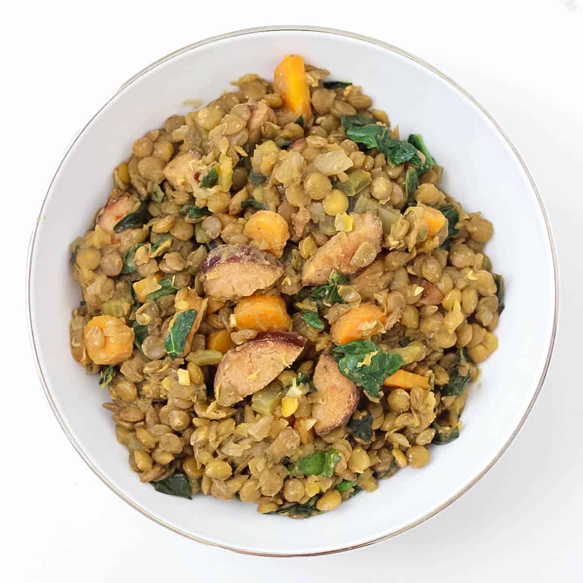 white counter with a white bowl full of lentils and sausage.