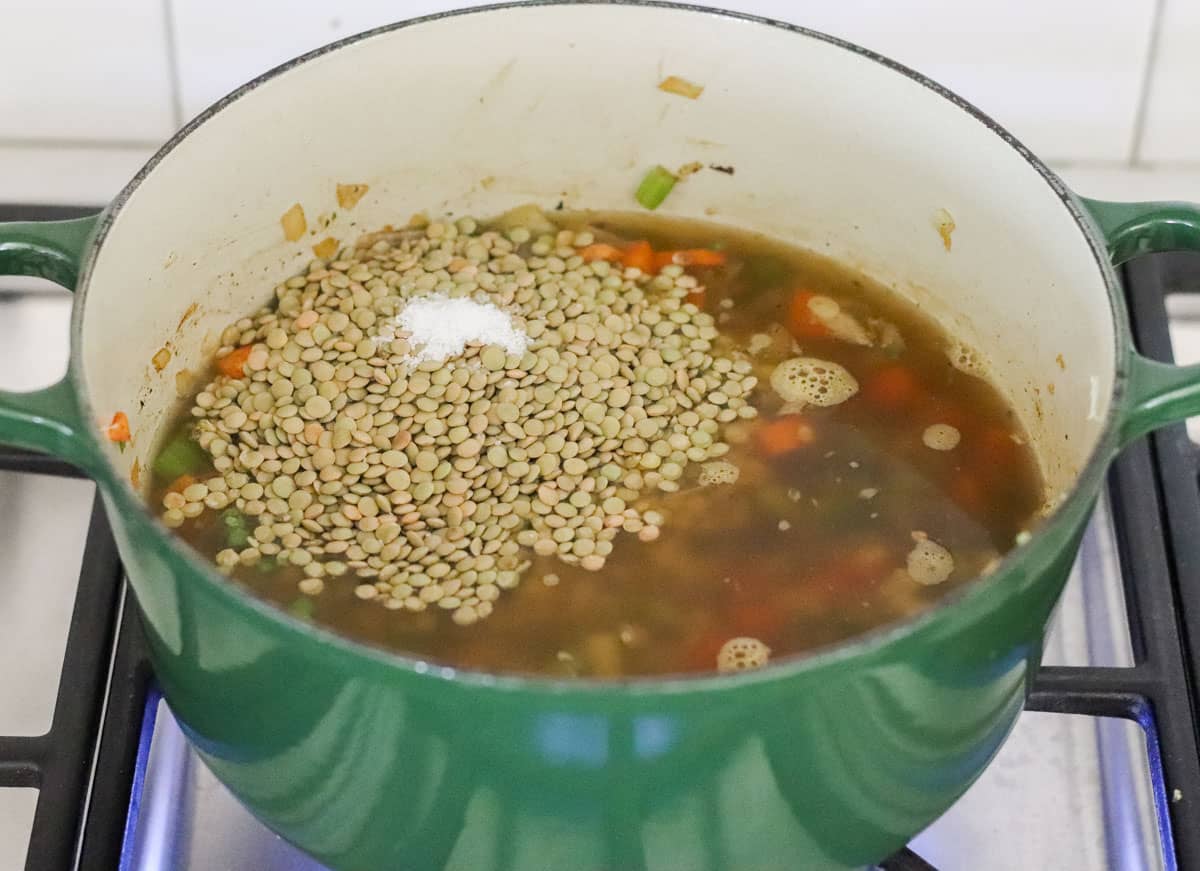 green pot with lentils, broth, and veggies cooking on a gas stove.